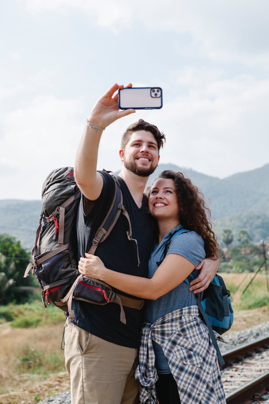 couple of travelers taking selfie on smartphone near grassy valley